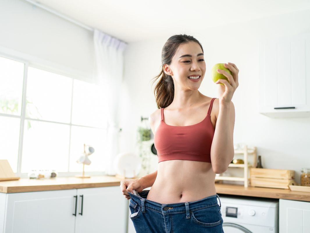 Mujer comiendo manzana y mostrando talla de pantalon